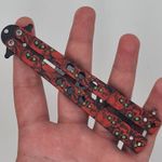 Sport si Outdoor - Camping - Cutite, bricege si accesorii - Cutite si bricege - Cutit fluture Butterfly, Balisong 21.50cm, cap de mort rosu M2, fara tais, de antrenament - Infinity.ro